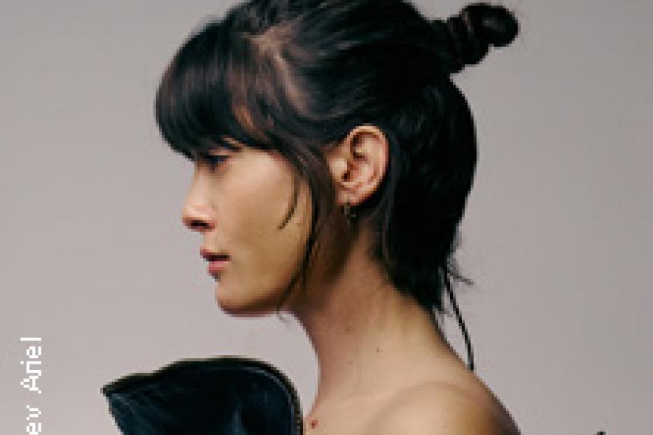 Eine Frau mit Pony und hochgesteckten Haaren, von der Seite fotografiert.