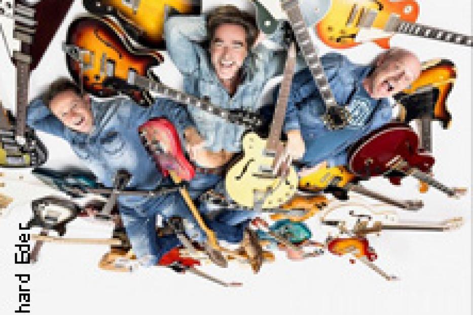 Drei Männer liegen auf dem Rücken, umgeben von vielen Gitarren.