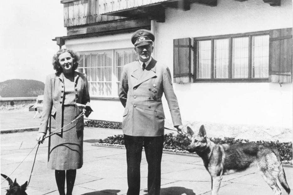 Eva Braun und Adolf Hitler mit Schäferhündin stehen auf der Terrasse des Berghofs.
