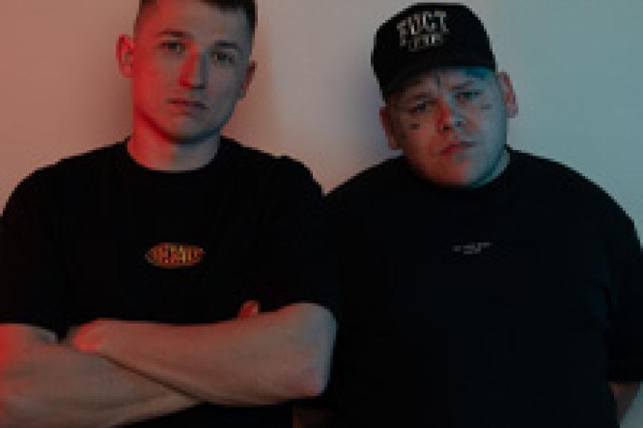 Zwei Männer stehen nebeneinander vor einer hellen Wand.