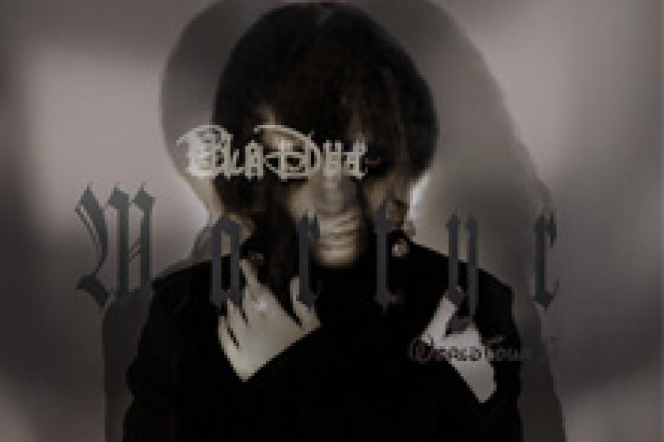 Ein verschwommenes Porträt einer Person in dunkler Kleidung vor einem grauen Hintergrund.