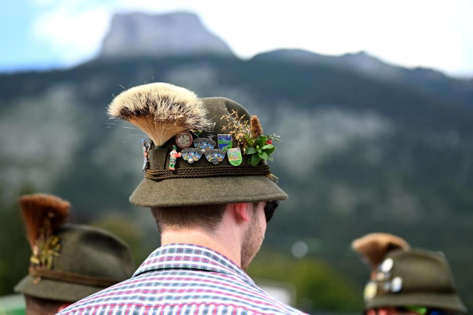 Ein Mann mit Hut mit Gamsbart und Ansteckern vor Bergkulisse