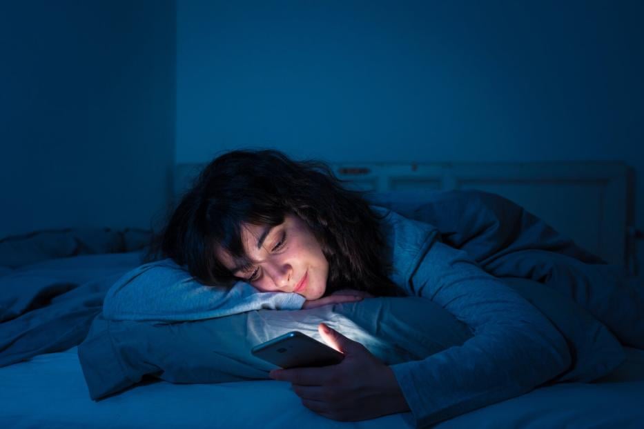 Frau in blauem Licht im Bett mit Handy 