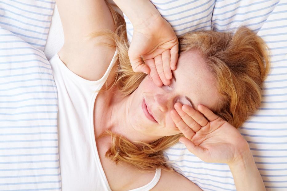 Frau um Bett reibt sich die Augen