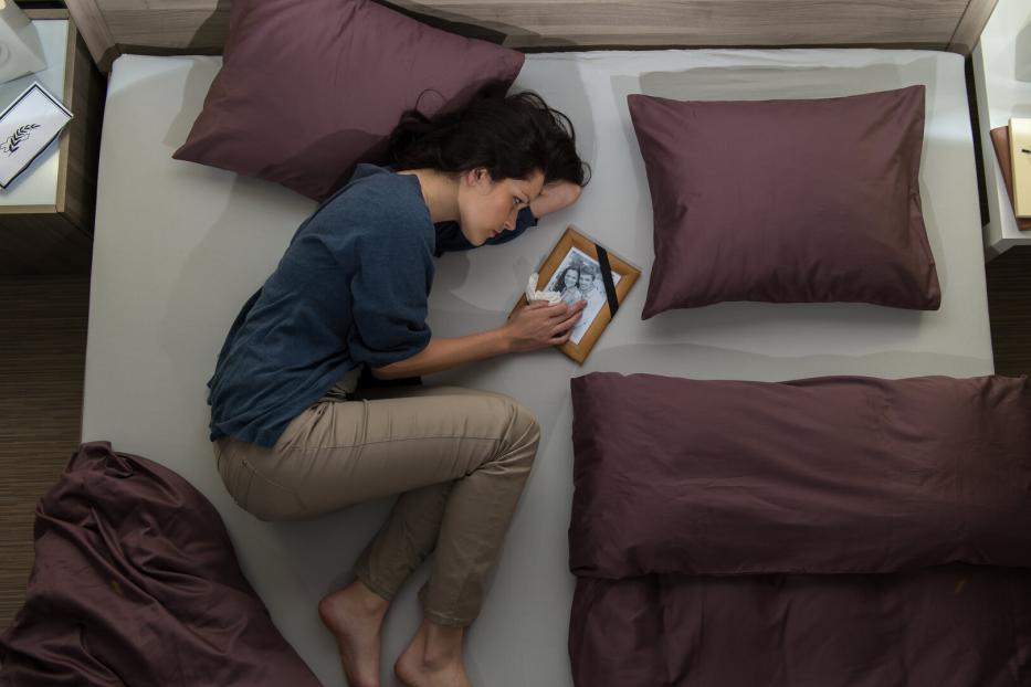 Trauernde Frau liegt mit Foto des verstorbenen am Bett