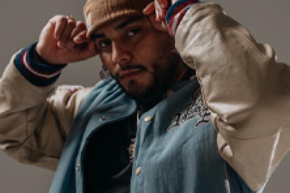 Ein Mann mit Bart und Mütze posiert in einer hellblauen Collegejacke.