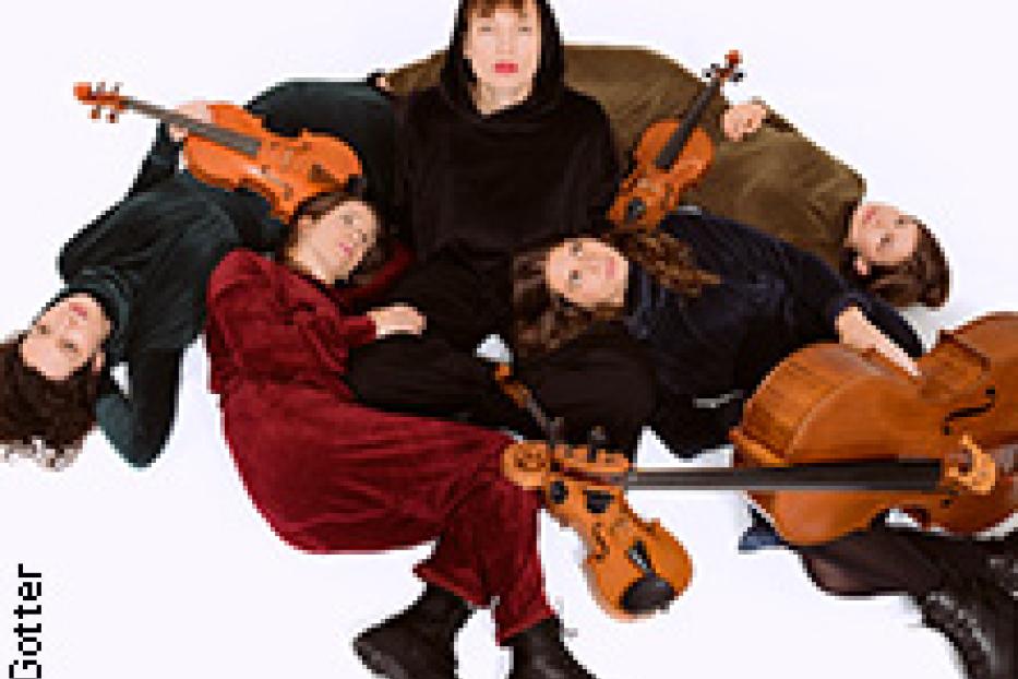 Eine Frau in schwarzer Kleidung sitzt inmitten von vier Frauen und Streichinstrumenten auf einem weißen Hintergrund.