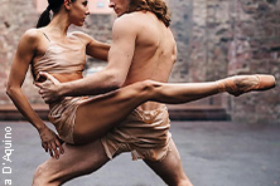 Zwei Balletttänzer posieren in einer innigen Umarmung vor einer Backsteinmauer.