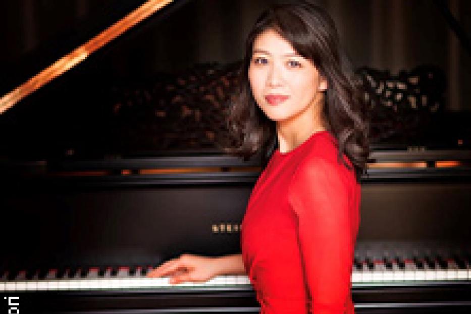 Eine Frau in einem roten Kleid sitzt an einem schwarzen Steinway-Flügel.