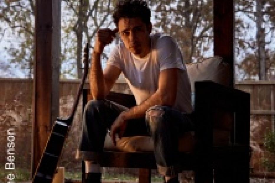 Ein Mann sitzt mit einer Gitarre auf einer Veranda.