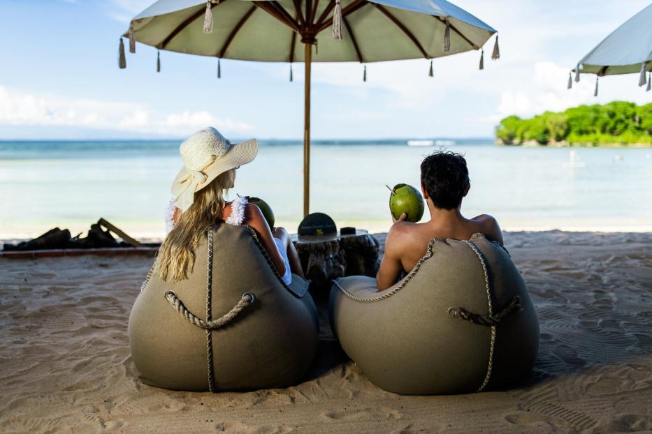 Rear view of a couple relaxing in bean bags on the beach.