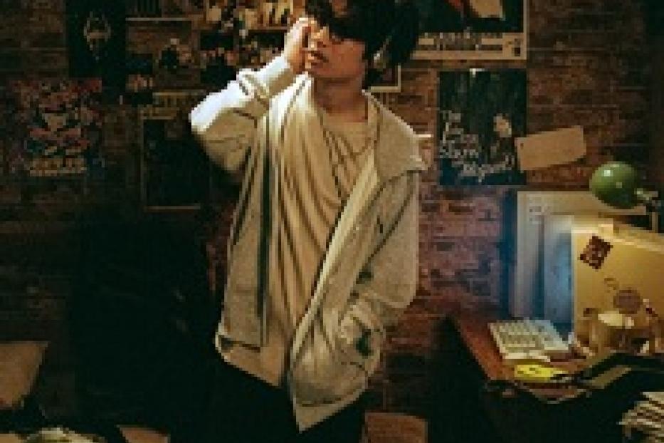 Ein junger Mann mit Brille steht in einem Zimmer mit vielen Postern an der Wand.