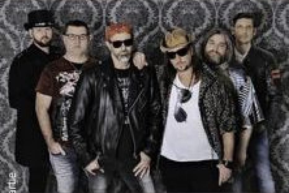 Eine Band posiert vor einer gemusterten Wand für ein Gruppenfoto.