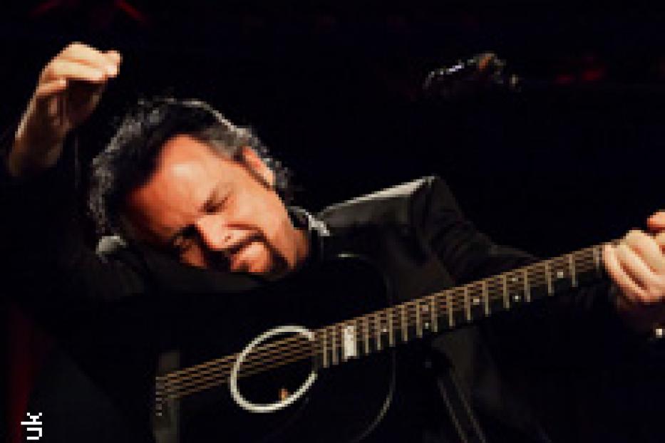Ein Mann mit Gitarre auf einer Bühne im dunklen Licht.
