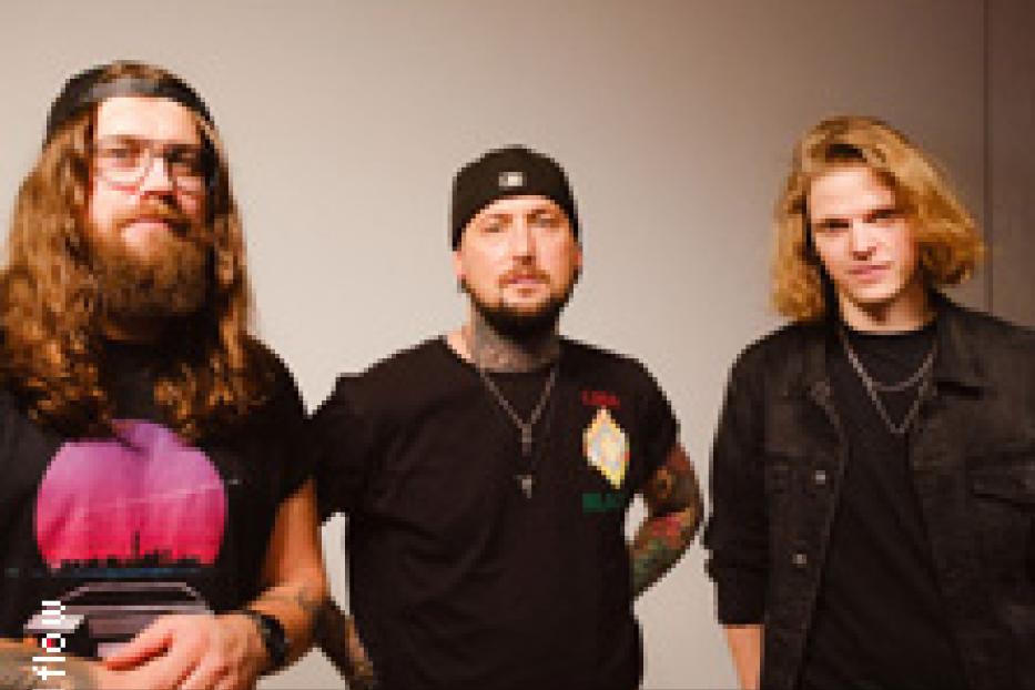 Drei Männer stehen vor einer grauen Wand.