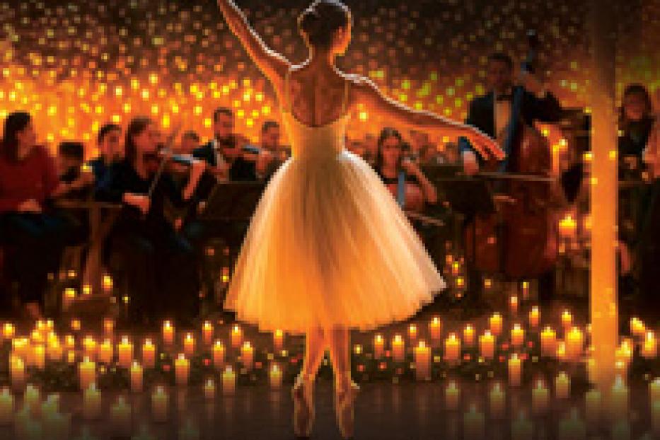 Eine Ballerina tanzt vor einem Orchester und vielen Kerzen, beworben als „Winterzauber“.