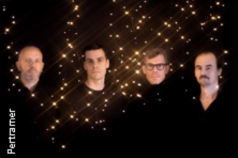 Vier Männer posieren vor einem dunklen Hintergrund mit goldenen Lichtern.