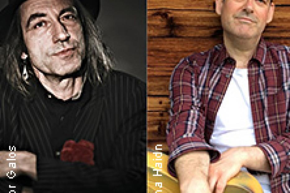 Ein Doppelporträt von zwei Männern, einer mit Hut und der andere mit Gitarre vor einer Holzwand.