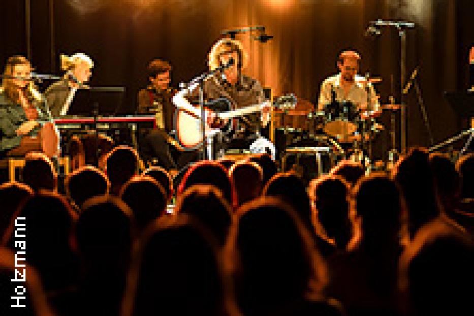 Eine Band spielt vor Publikum auf einer Bühne mit Scheinwerfern.
