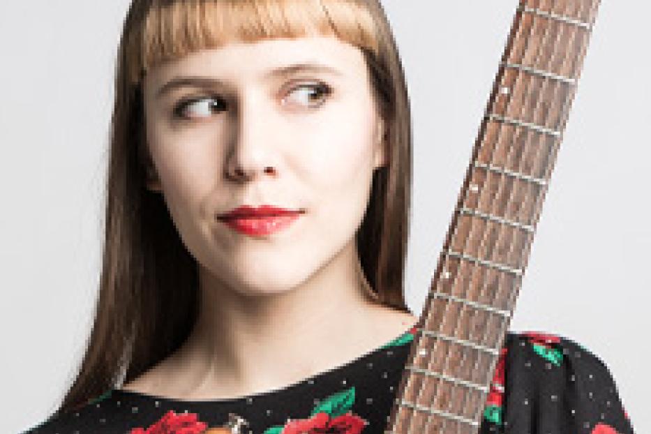 Eine junge Frau mit Pony und rotem Lippenstift hält eine E-Gitarre.