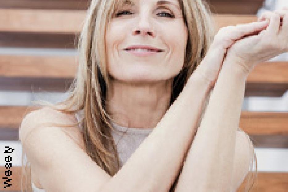 Eine Frau mit blonden Haaren sitzt lächelnd auf einer Holztreppe.
