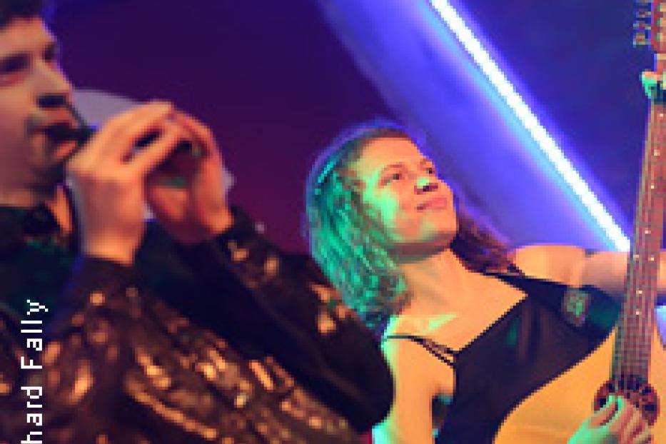 Eine Frau mit Gitarre und ein Mann mit einem Blasinstrument treten auf einer Bühne auf.