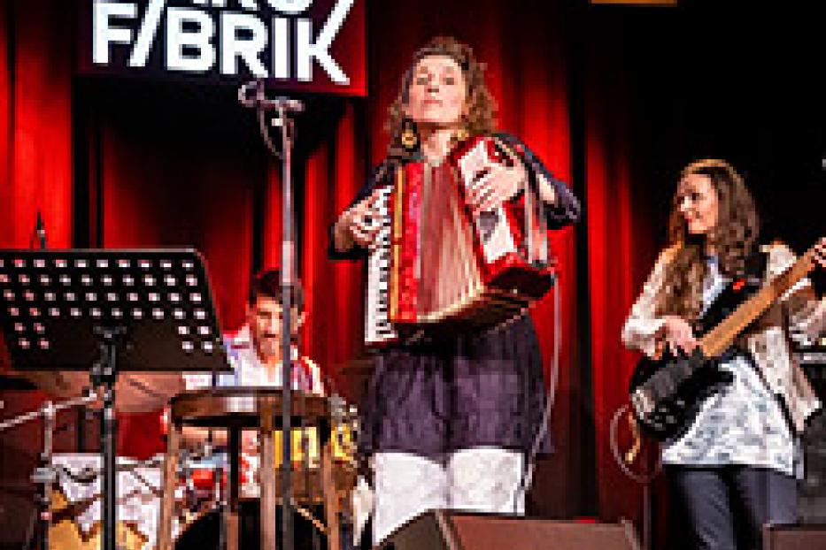 Eine Frau spielt Akkordeon auf einer Bühne, begleitet von einer Band.