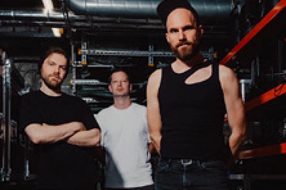 Drei Männer stehen vor einer technischen Installation.