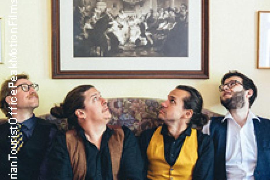 Vier Männer sitzen auf einem Sofa und schauen nach oben.