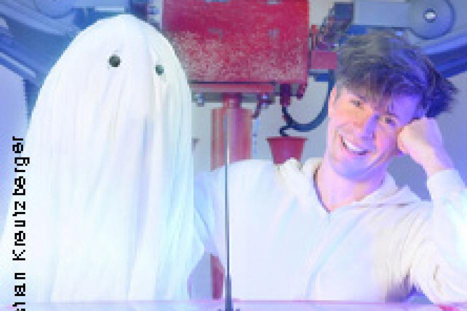 Ein Mann lächelt neben einem als Geist verkleideten Kind oder einer Puppe.