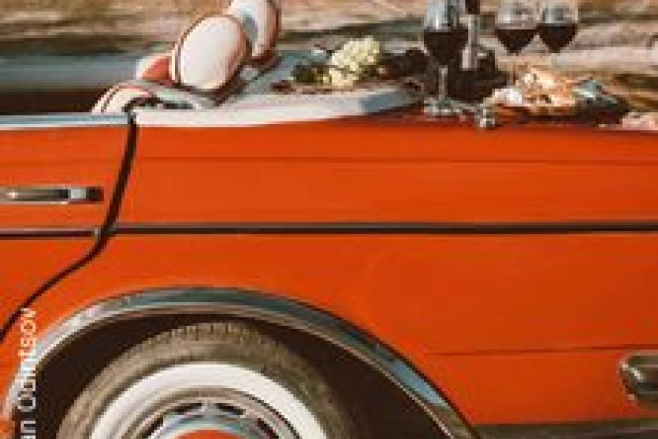 Ein rotes Cabriolet mit Wein, Gläsern und Snacks auf der Kofferraumhaube.