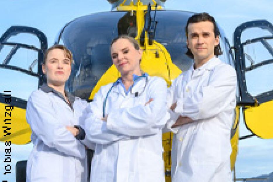 Drei Sanitäter stehen vor einem gelben Rettungshubschrauber.