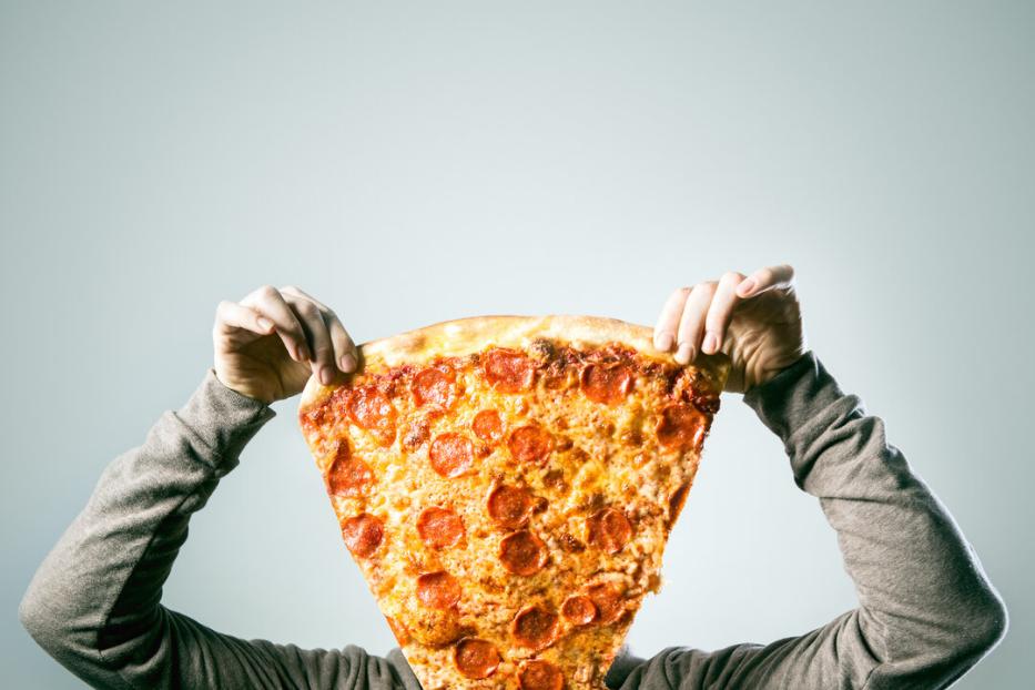 Mann hält eine riesige Pizzaschnitte vor sein Gesicht