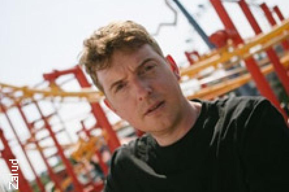Ein Mann mit blonden Haaren vor einer Achterbahn.