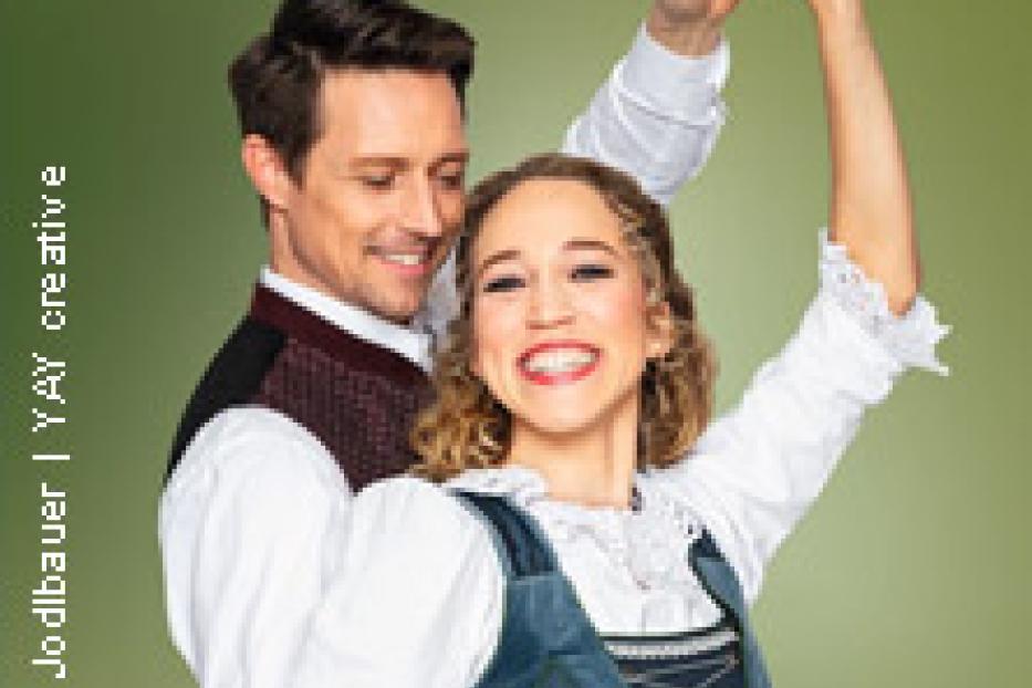 Ein lächelndes Paar in Tracht posiert vor einem grünen Hintergrund.