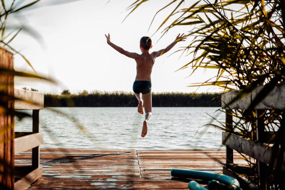 Young boy having fun enjoying a summer day jumping at the lake.