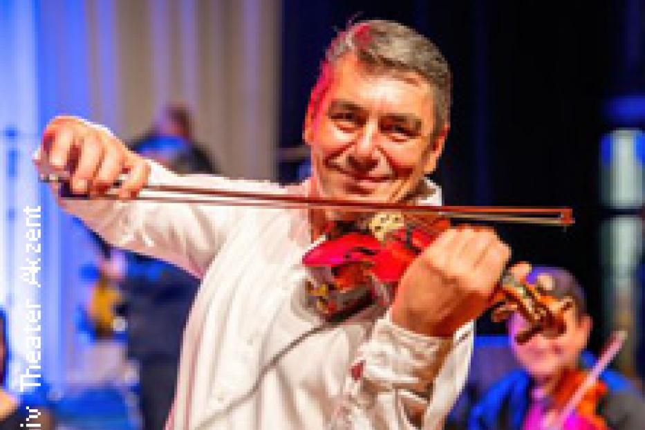 Ein lächelnder Mann spielt auf einer Bühne Geige.