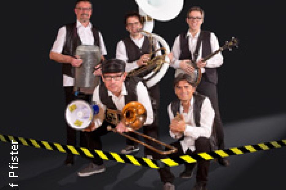 Eine Band mit Blasinstrumenten posiert vor einem dunklen Hintergrund.