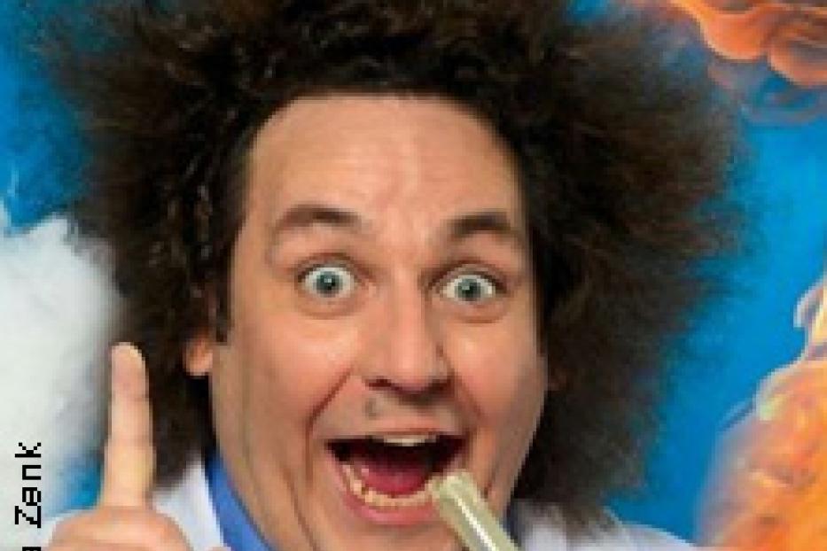 Ein Mann mit wilder Frisur und einem Laborkittel hält ein Reagenzglas und hat eine Idee.