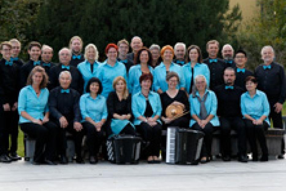 Ein gemischter Chor in blauen Hemden und schwarzen Hosen posiert für ein Gruppenfoto.