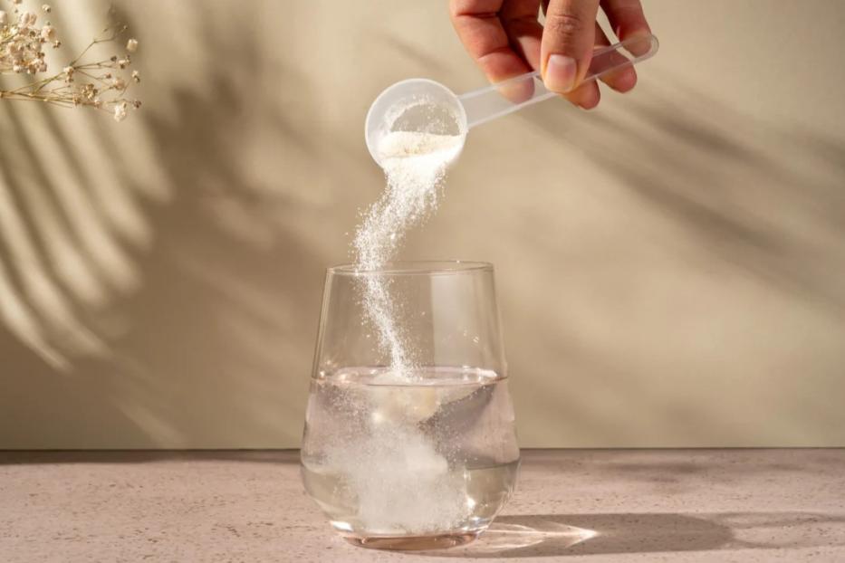 Eine Person kippt einen Löffel mit Basenpulver in ein Glas Wasser zum Auflösen.