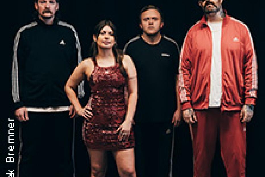 Eine Band posiert vor einem schwarzen Hintergrund, alle tragen Trainingsanzüge oder sportliche Kleidung.