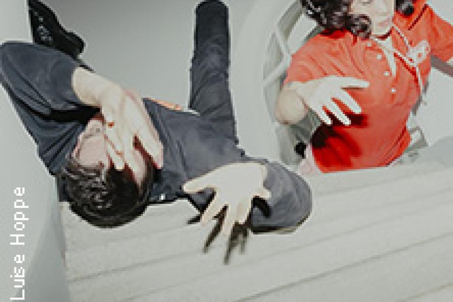 Eine Person fällt eine Treppe hinunter, während eine andere Person durch ein rundes Fenster schaut.