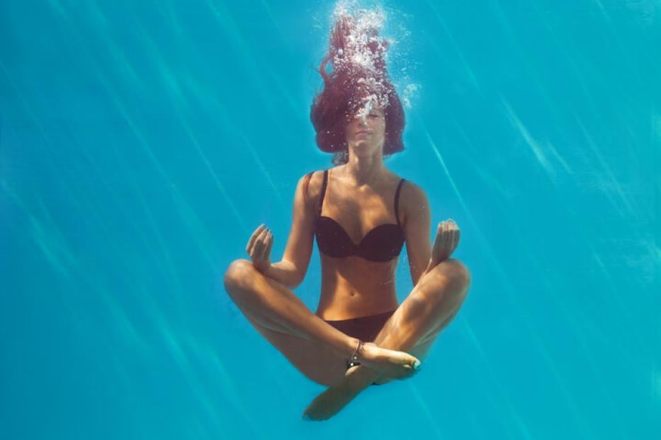 Frau schwebt in Yogaposition in einem Pool unter Wasser