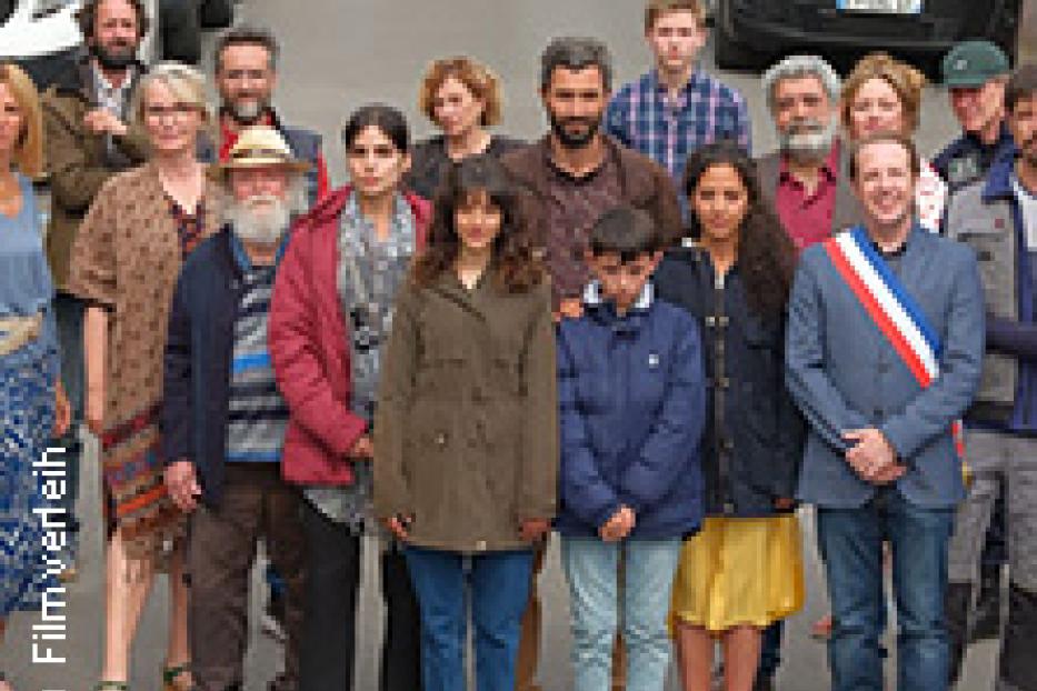 Eine Gruppe von Menschen steht auf einer Straße vor geparkten Autos.