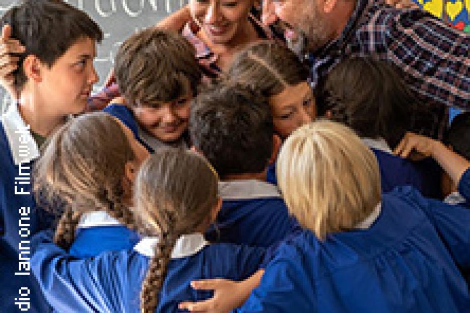 Eine Gruppe von Schulkindern umarmt ihre Lehrerin und ihren Lehrer.