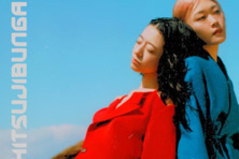 Zwei Frauen stehen Rücken an Rücken vor einem blauen Himmel.