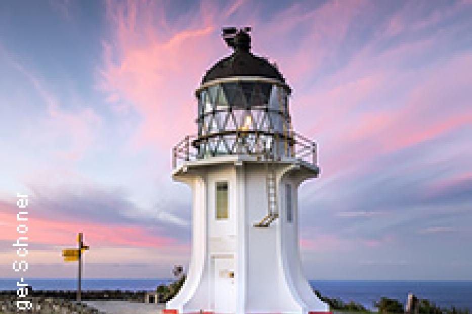 Ein weißer Leuchtturm steht vor einem Himmel in Rosa- und Blautönen.