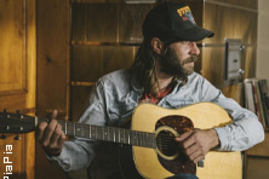 Ein Mann mit Bart und Mütze spielt Gitarre.