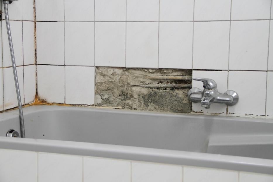 An old bathroom with broken white tiles and mold